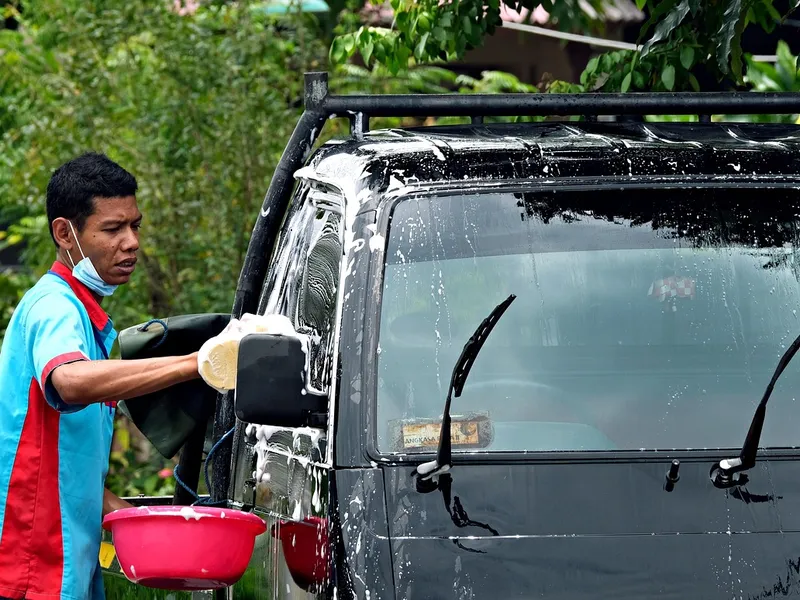 Person hand washing a vehicle with a bucket of soapy water