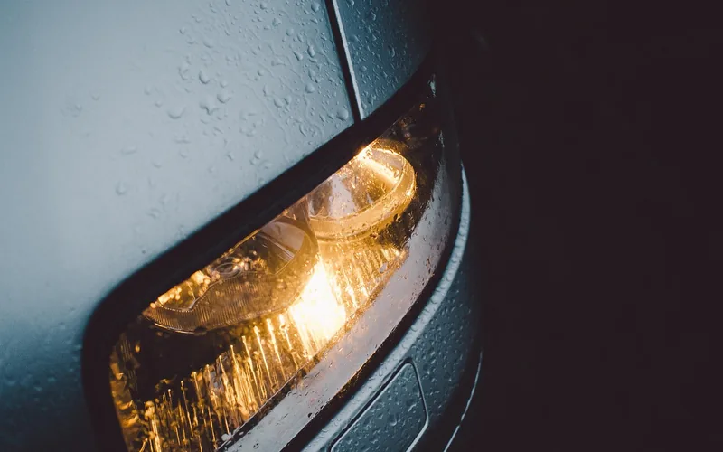 Car headlight lit with water droplets on the body panel