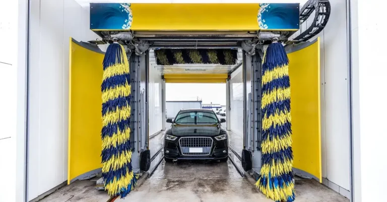Dark SUV entering an automatic car wash bay with yellow and blue rotating brushes