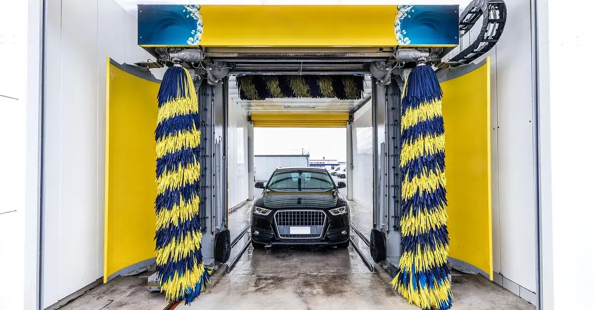 Dark SUV entering an automatic car wash bay with yellow and blue rotating brushes