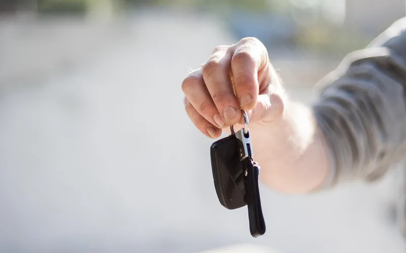 Hand holding a car key on a ring against a blurred outdoor background Hand holding a car key on a ring against a blurred outdoor background