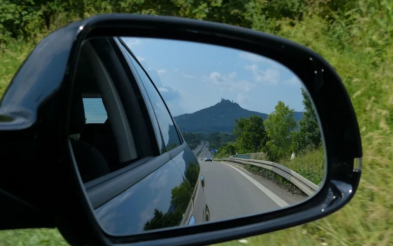 Car side mirror showing the road and a following vehicle behind