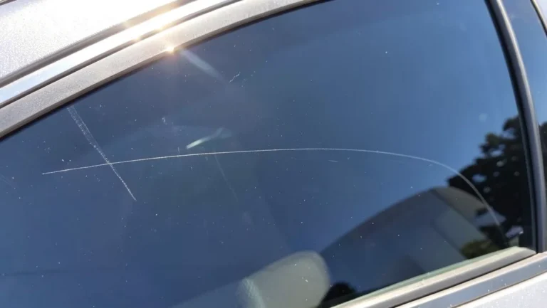 Close-up of a thin scratch on a car side window glass in sunlight