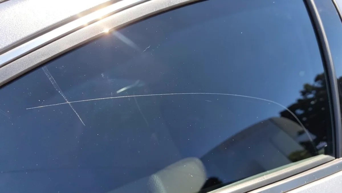 Close-up of a thin scratch on a car side window glass in sunlight