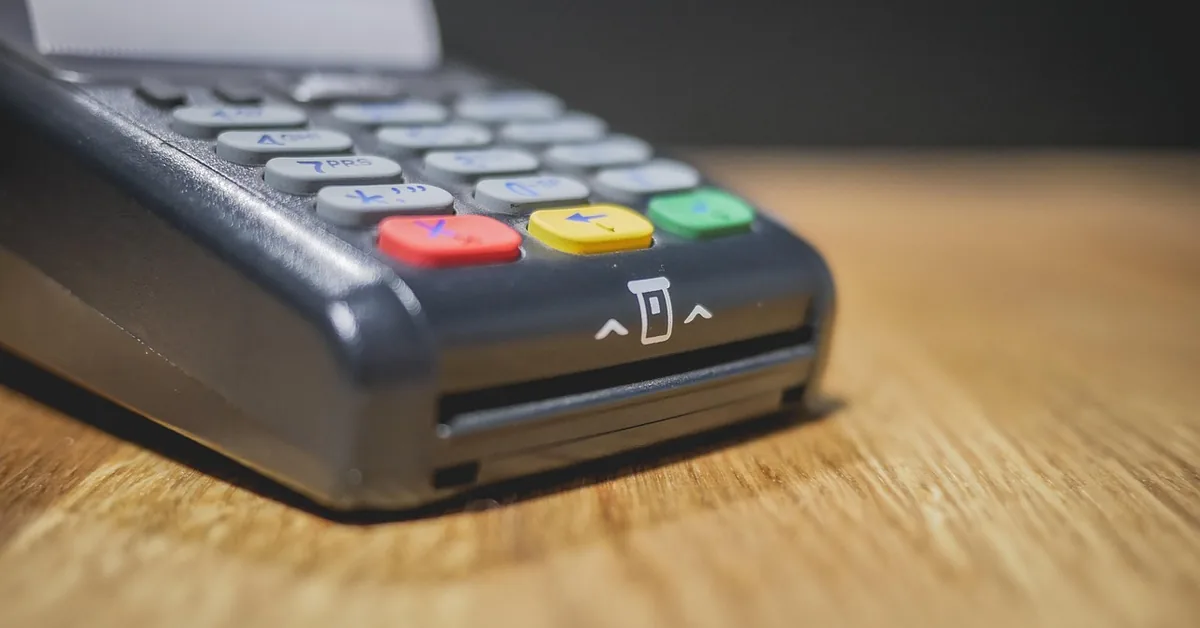 Close-up of a card payment terminal with number keys and a card slot on a wooden counter
