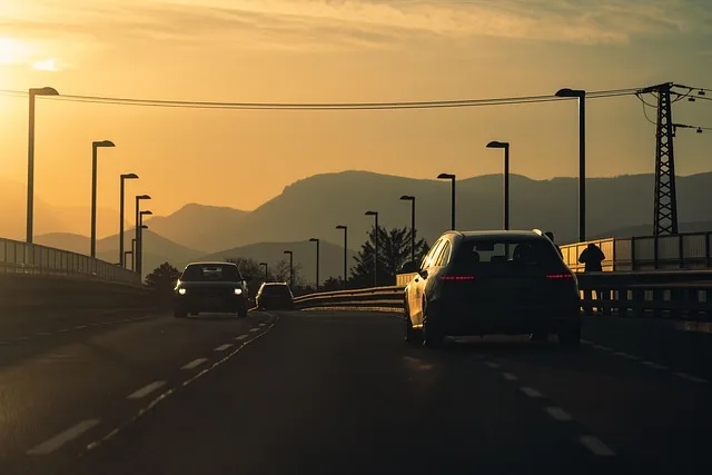 Cars driving on a highway bridge toward mountains at sunset