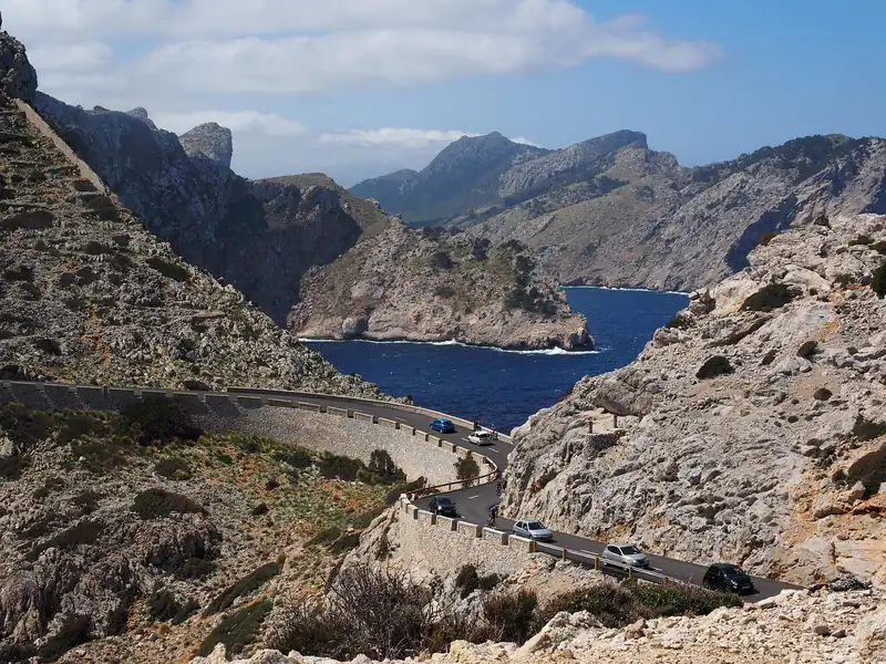 Cars driving a winding mountain road along a cliff above a bay