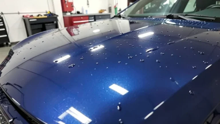 Glossy dark blue car hood with ceramic coating causing water to bead and roll off the surface