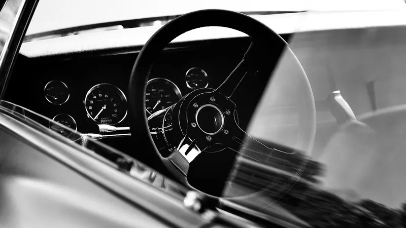 Black and white view of a classic car steering wheel and dashboard gauges
