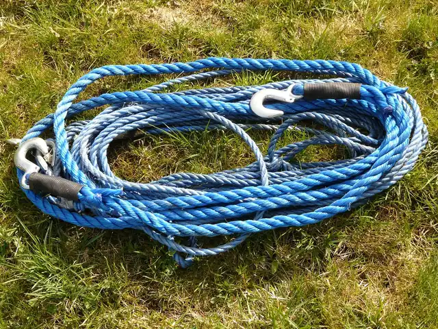 Coiled blue tow rope with metal hooks lying on grass