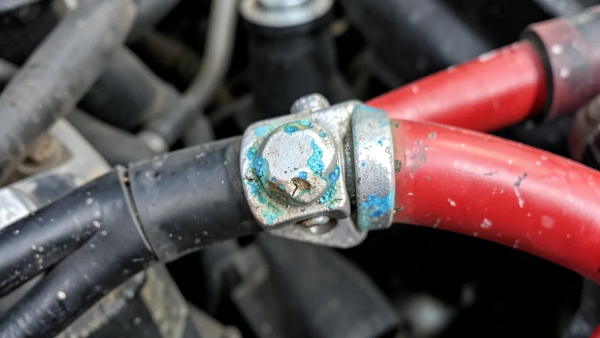 Close-up of a corroded car battery cable terminal clamp with visible white and blue-green buildup