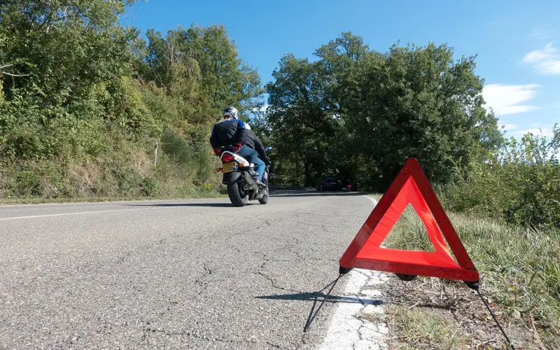 A red reflective warning triangle standing on the shoulder of a highway