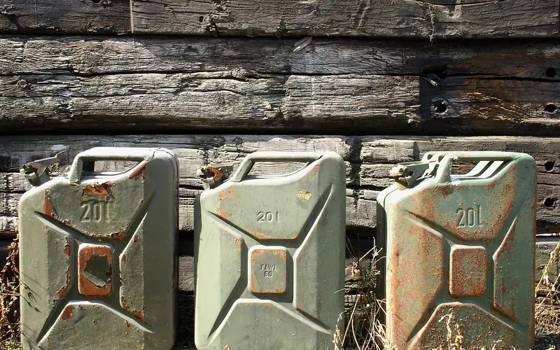 Three metal jerry cans standing against a weathered wooden wall Three metal jerry cans standing against a weathered wooden wall