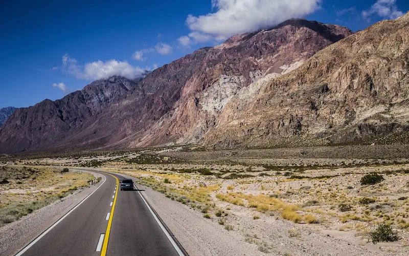Two-lane road running through dry mountain terrain with a single car Two-lane road running through dry mountain terrain with a single car