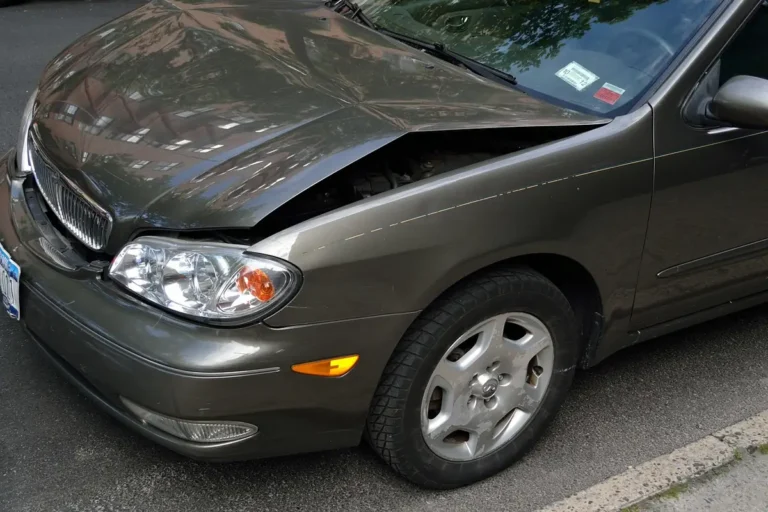 Car with a dented hood and damaged front bumper area parked at a curb