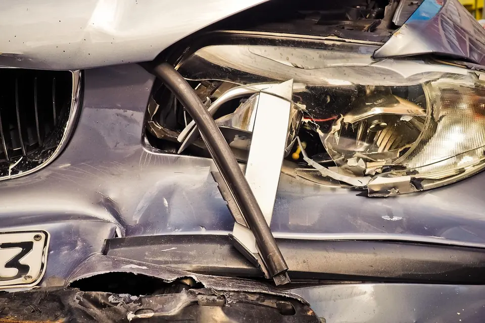 Close-up of a crash-damaged front corner with a broken headlamp and torn bumper cover