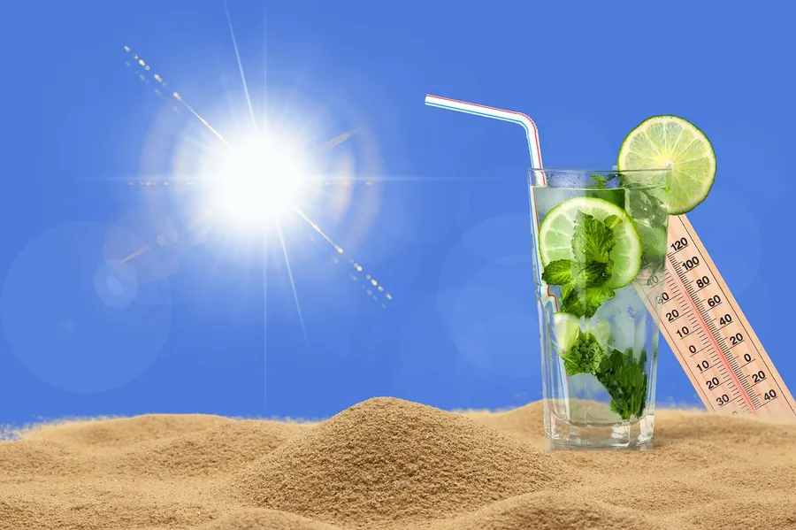 Bright sun over sand beside a drink and an outdoor thermometer