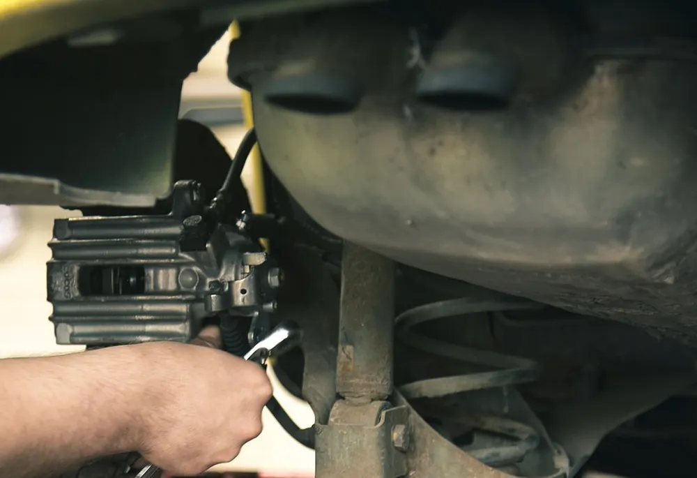 Mechanic holding a wrench at a rear brake caliper on a lifted car