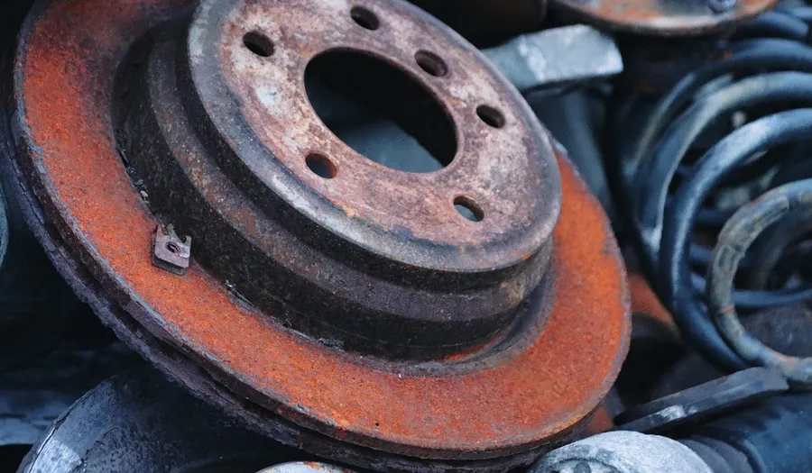 Heavily rusted brake rotor lying among scrap suspension parts