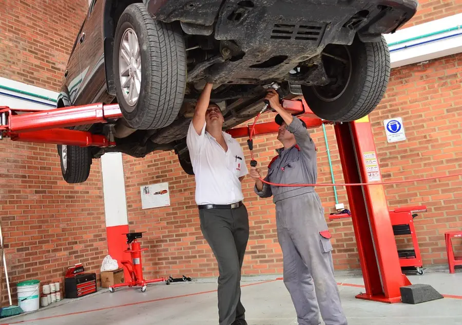 Two mechanics working under a car raised on a two-post lift in a shop