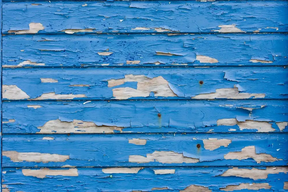 Flaking blue paint on weathered boards with bare wood showing where the paint has come off