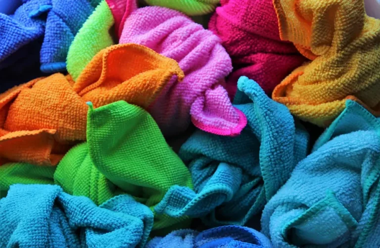 Pile of folded and crumpled microfiber cloths in blue, green, orange, pink and yellow