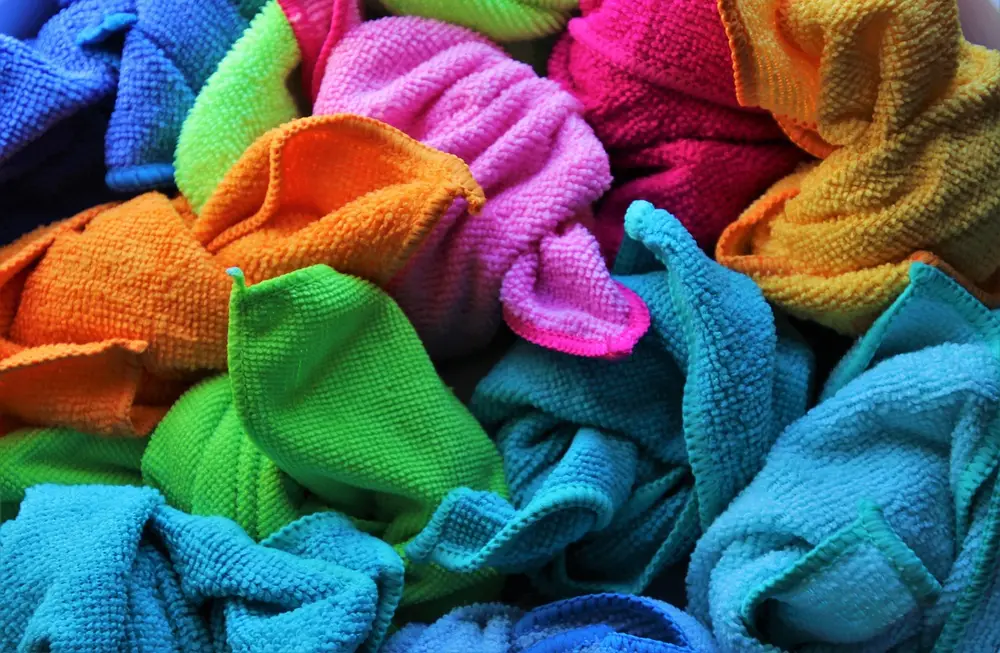 Pile of folded and crumpled microfiber cloths in blue, green, orange, pink and yellow