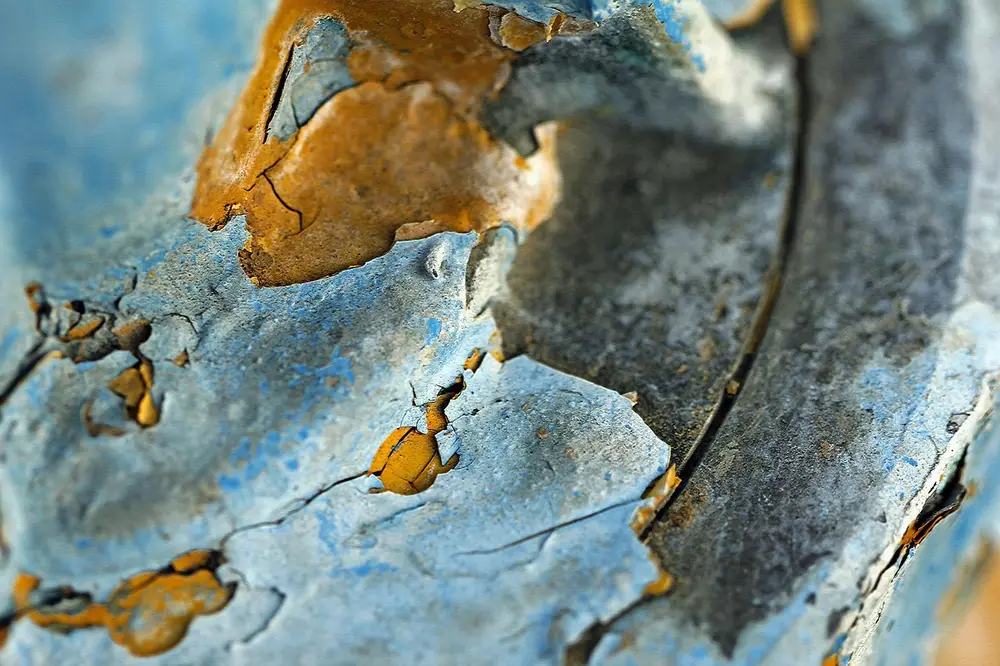 Close-up of peeling blue paint on a metal object with an orange layer showing underneath