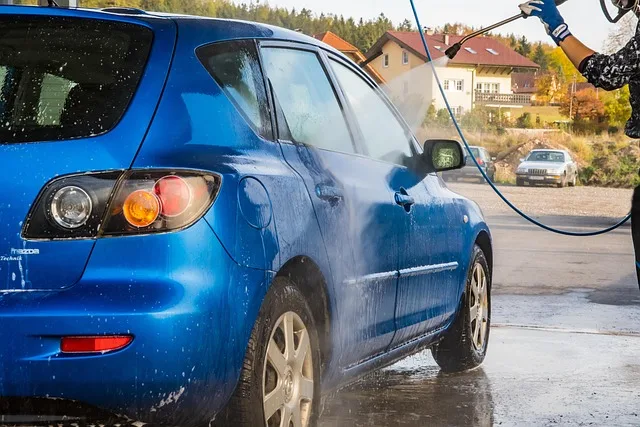 Washing a blue hatchback with a hose and soap in a home driveway using the DIY two-bucket method