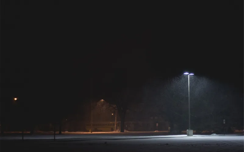 Empty parking lot at night under a single street light with light snow