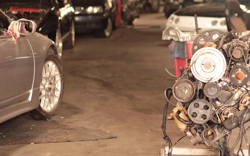Repair garage floor with an engine on a stand beside parked cars
