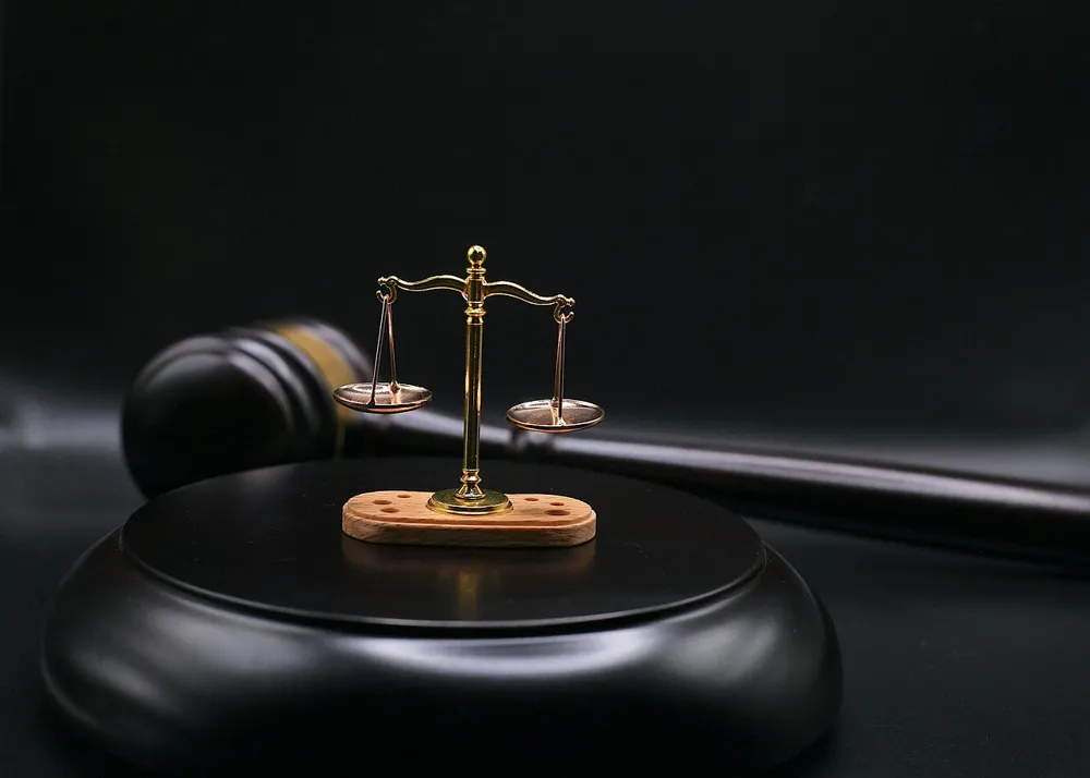 Small brass scales of justice on a wooden base in front of a black gavel and sound block