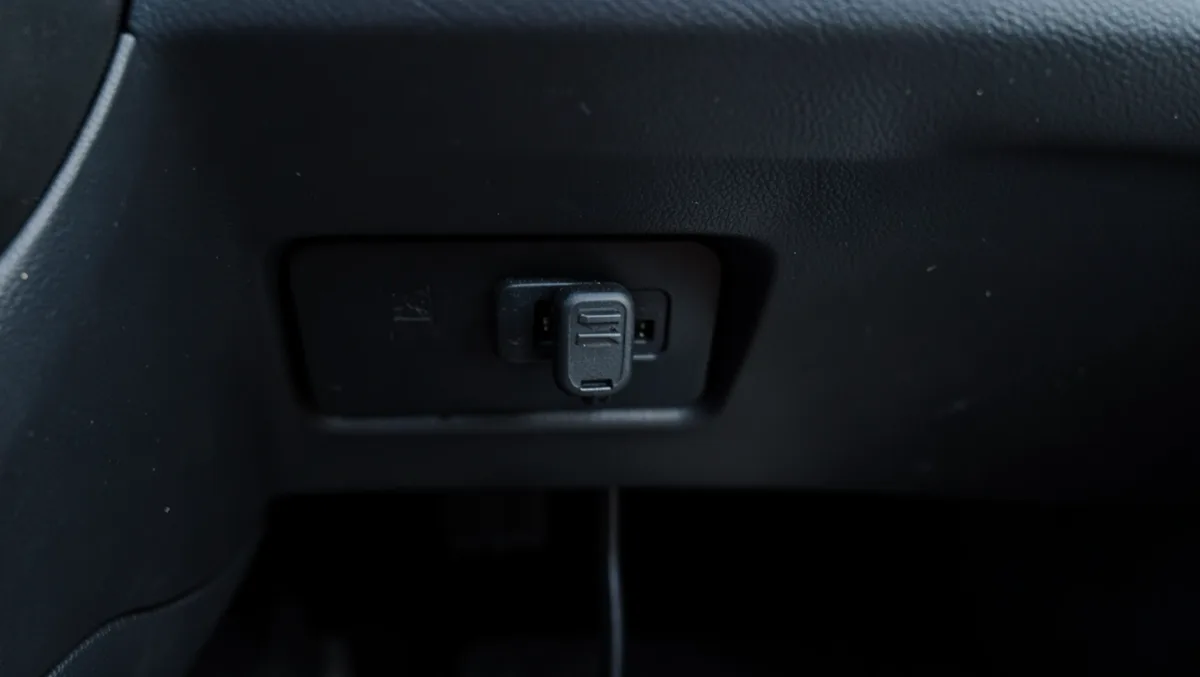 Small black GPS tracker module clipped near the OBD-II port under a car dashboard