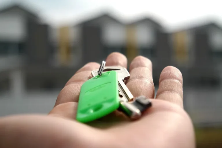 Hand holding a set of keys with a green tag in front of blurred buildings