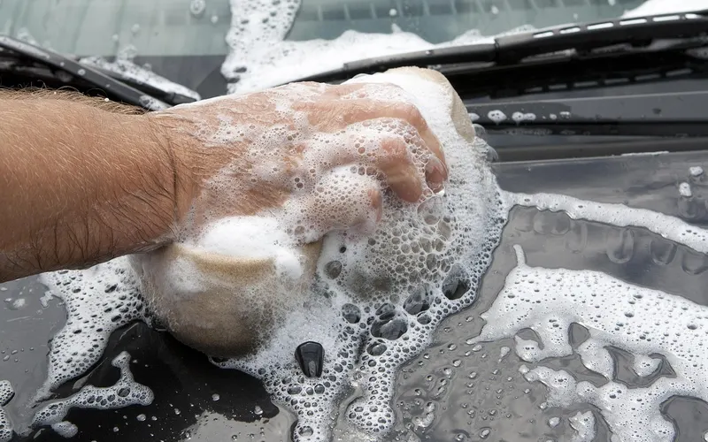 Hand washing a car hood with a foamy sponge
