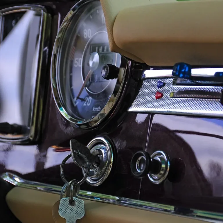 Keys hanging from the ignition lock on a vintage car dashboard next to a speedometer