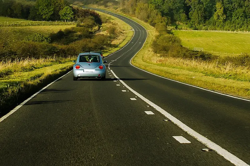 Small blue car driving along a winding country road