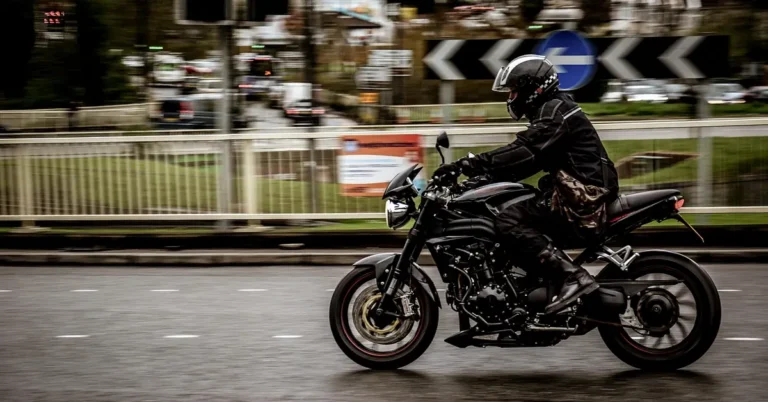 Motorcyclist in a black jacket and helmet riding past on a wet city road
