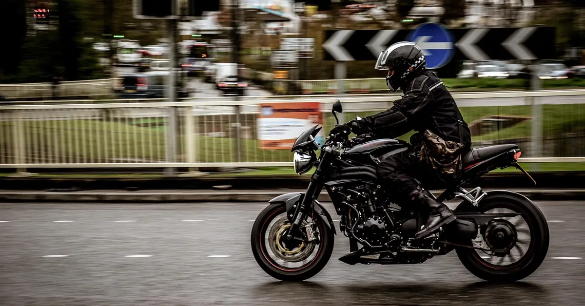 Motorcyclist in a black jacket and helmet riding past on a wet city road