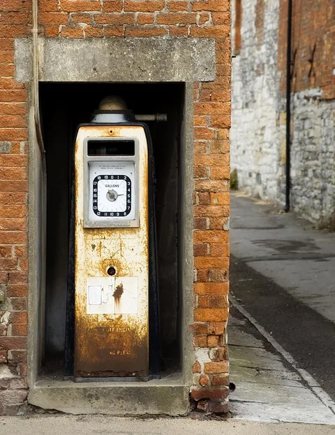 Weathered fuel pump with a gallons dial set into a brick wall niche