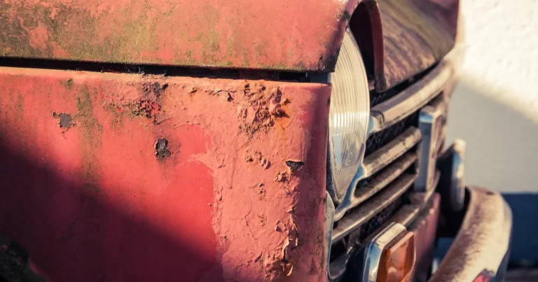 Faded, chalky and flaking red paint on the front fender of an old car