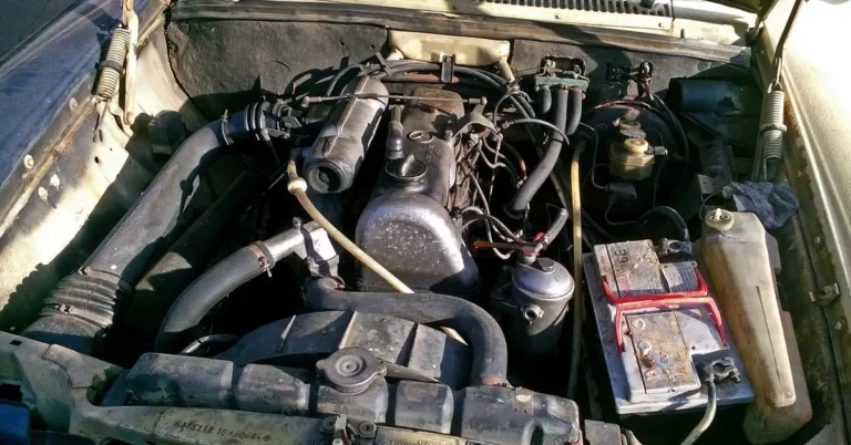 Engine bay of an older car with the battery mounted on a tray beside the coolant tank