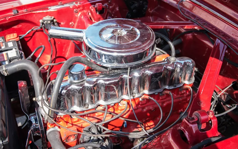 Engine bay of an older car with a chrome air cleaner, ignition wires and hoses crossing the engine