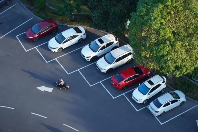 Cars in marked parking spaces seen from above, with a scooter crossing the lot