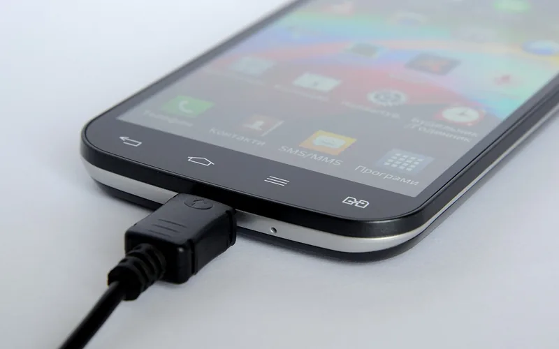 A smartphone connected to a black USB cable plug at its charging port
