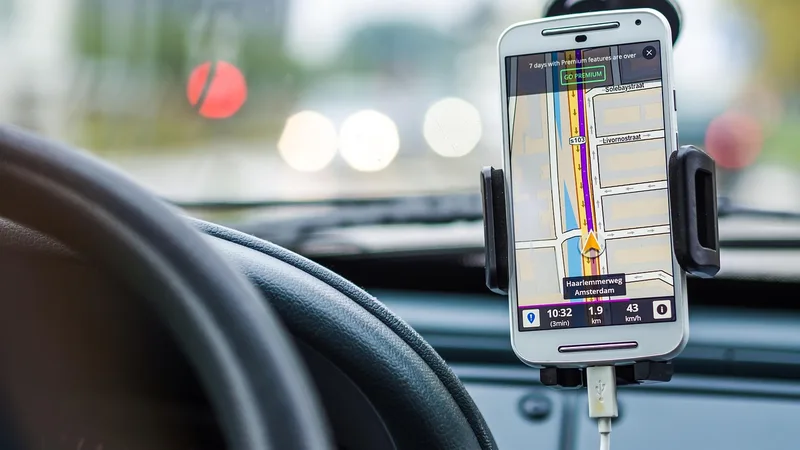 Smartphone in a dashboard mount showing a navigation map with a charging cable plugged in