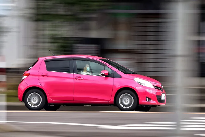 Pink hatchback driving along a road with motion blur