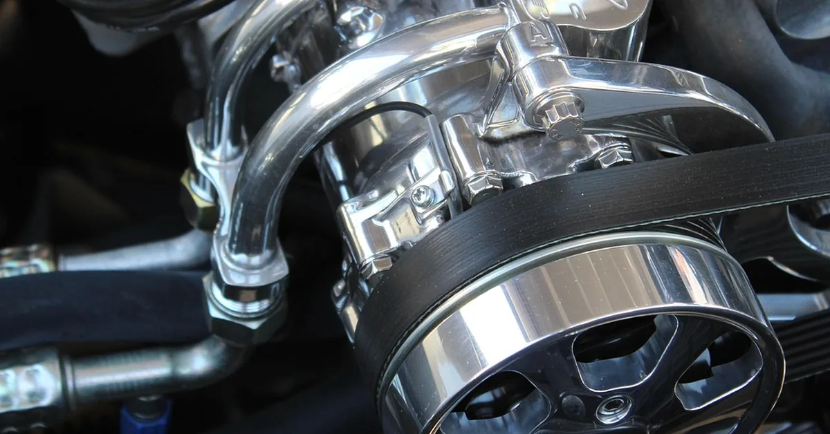 Polished engine pulley with a black ribbed drive belt and hoses beside it