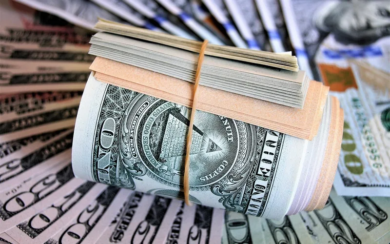 Roll of US dollar bills held with a rubber band on top of loose bills