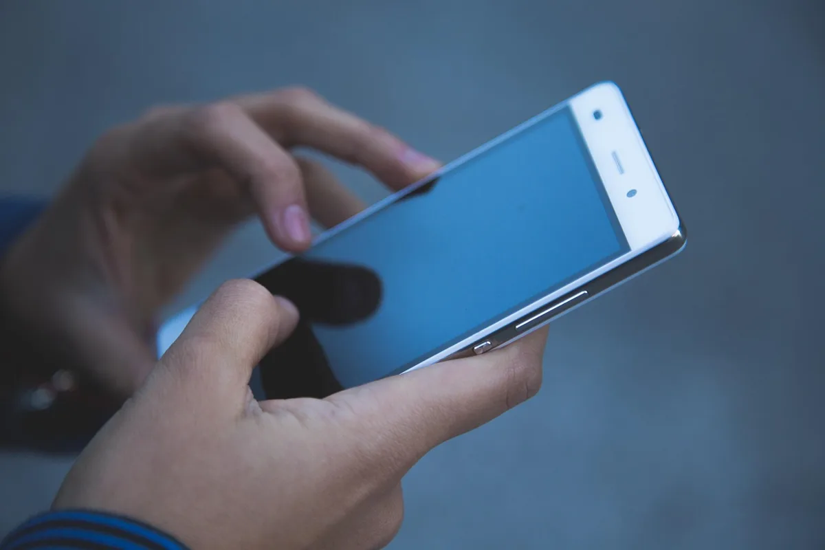 Hands holding a white smartphone with a blank screen